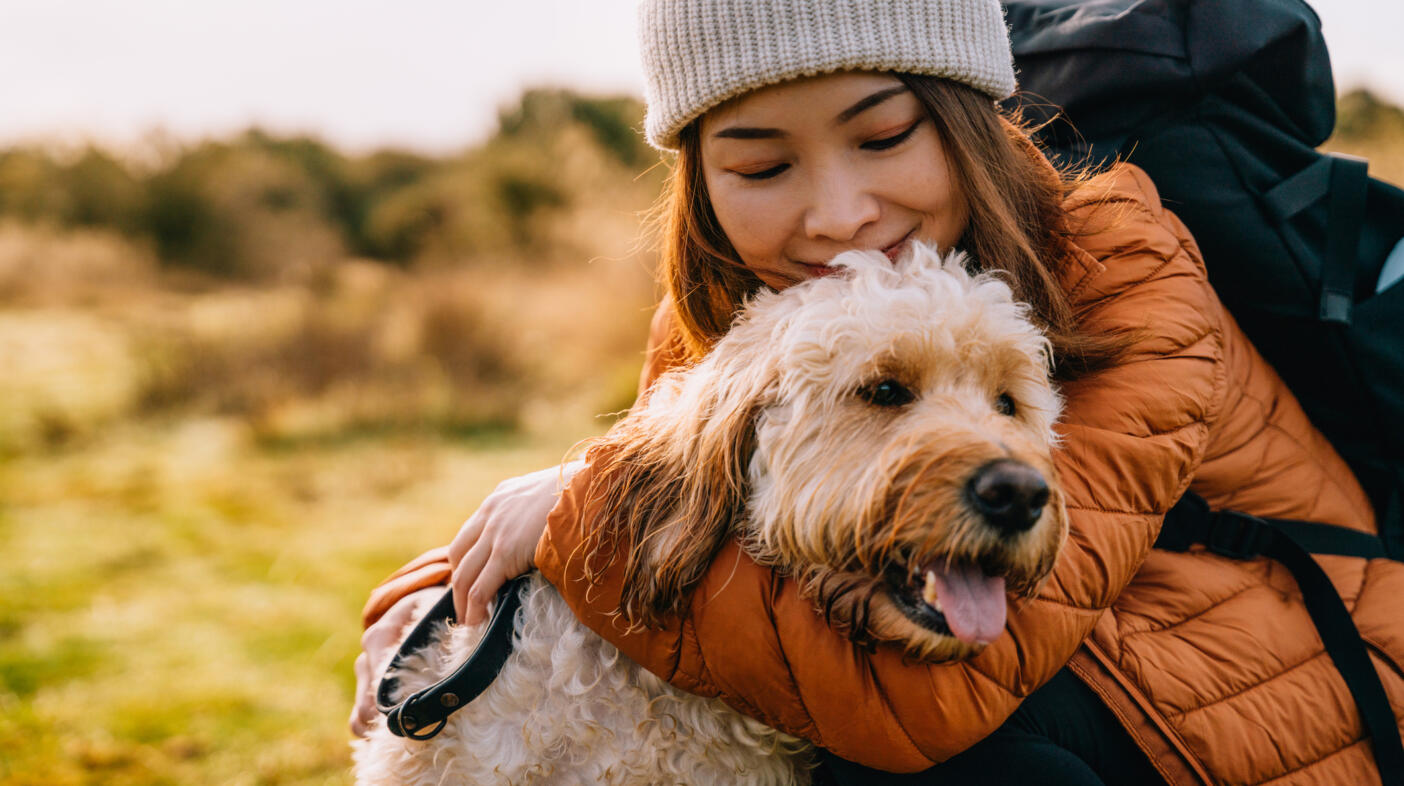 Young Asian woman hugging her dog while hiking in autumn nature.